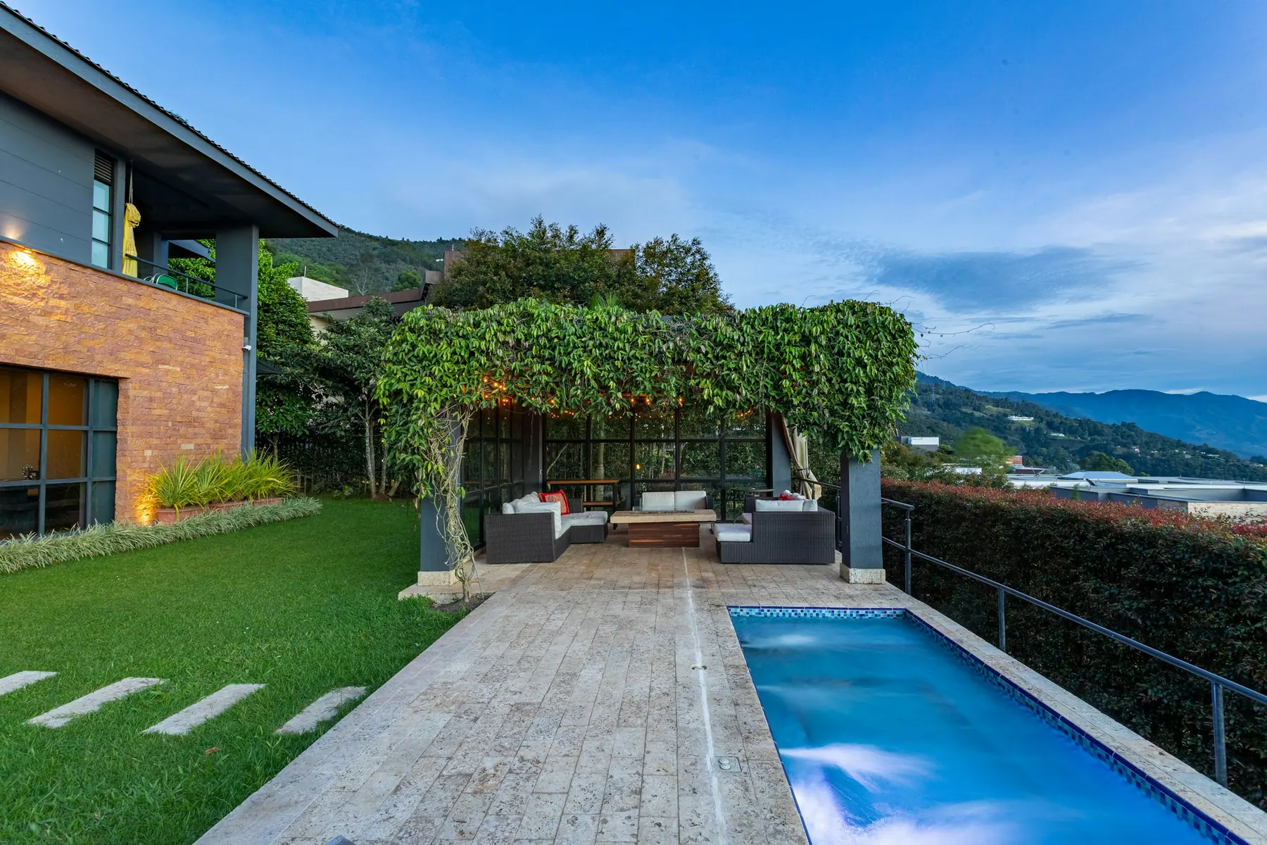 Piscina com deque de madeira e pérgola coberta por vegetação, com vista para as montanhas