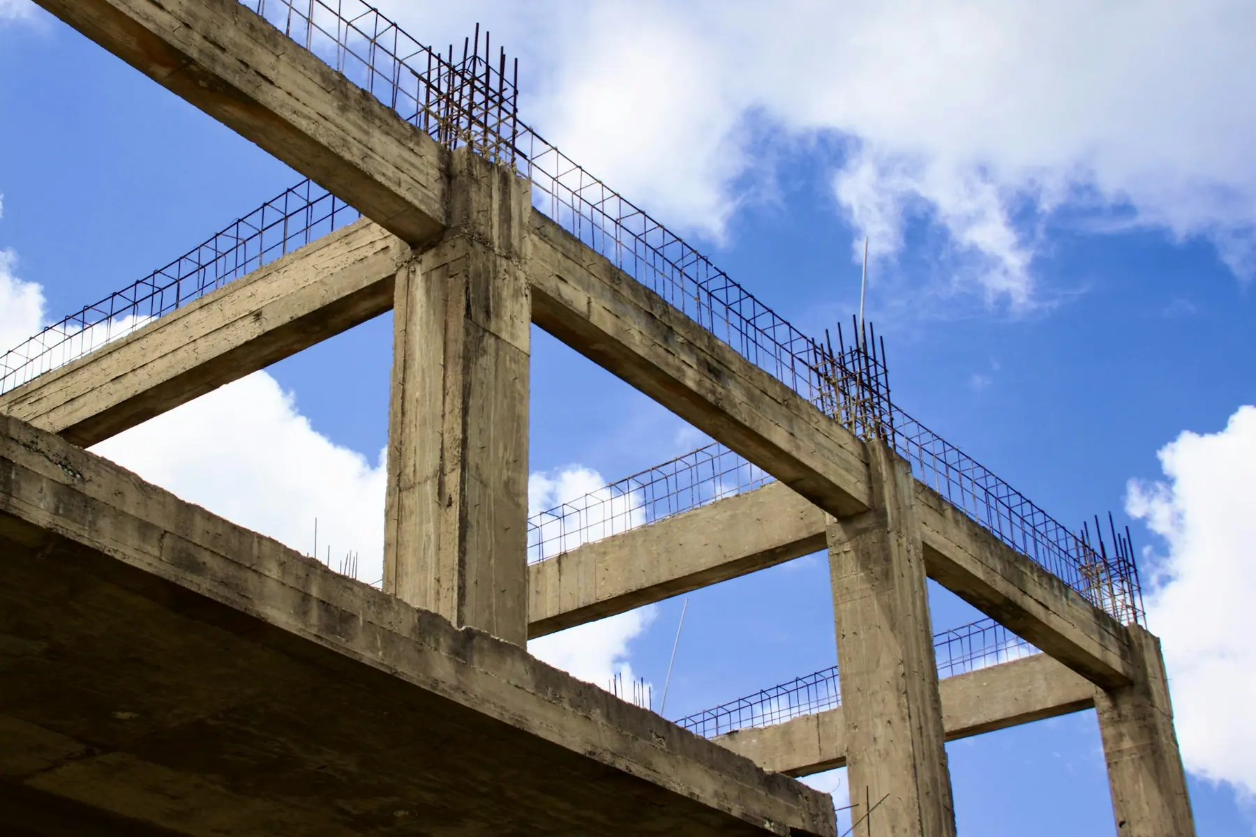 Pilares e vigas de concreto com armaduras expostas contra o céu